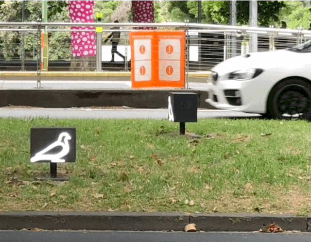 a small sign of an electronic pigeon pecking at the ground with cars going past